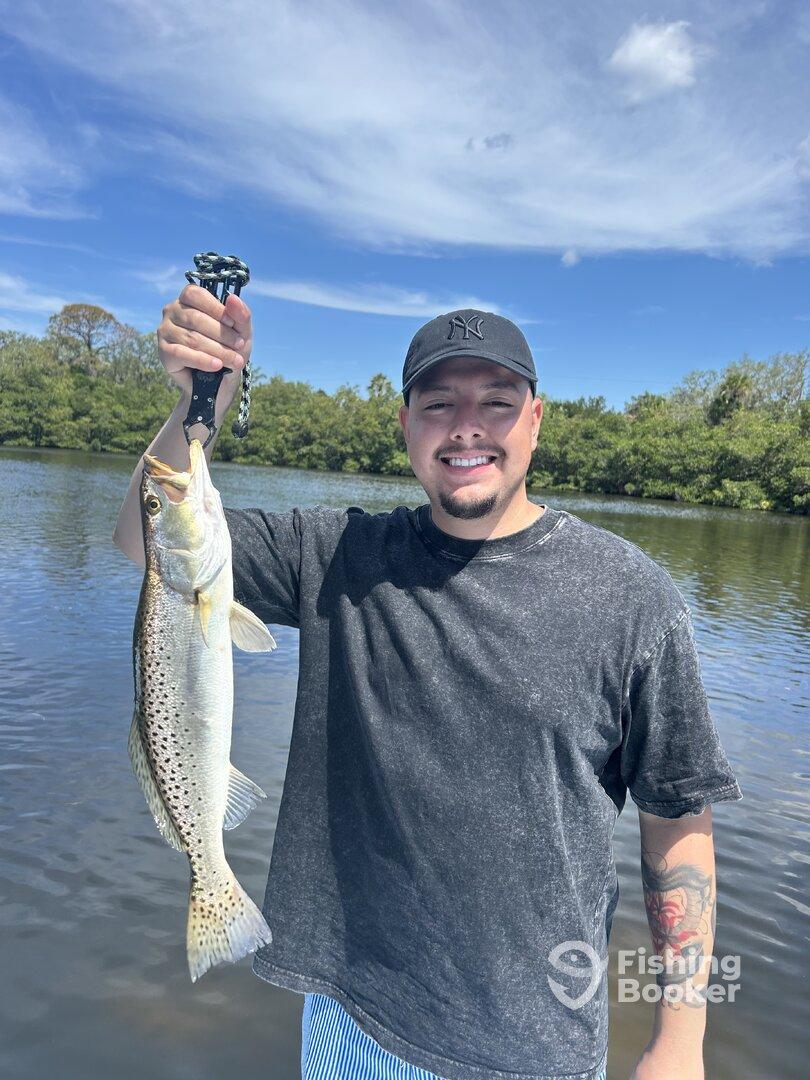 Angler proudly displaying a large Speckled Trout while fishing in a scenic waterway.