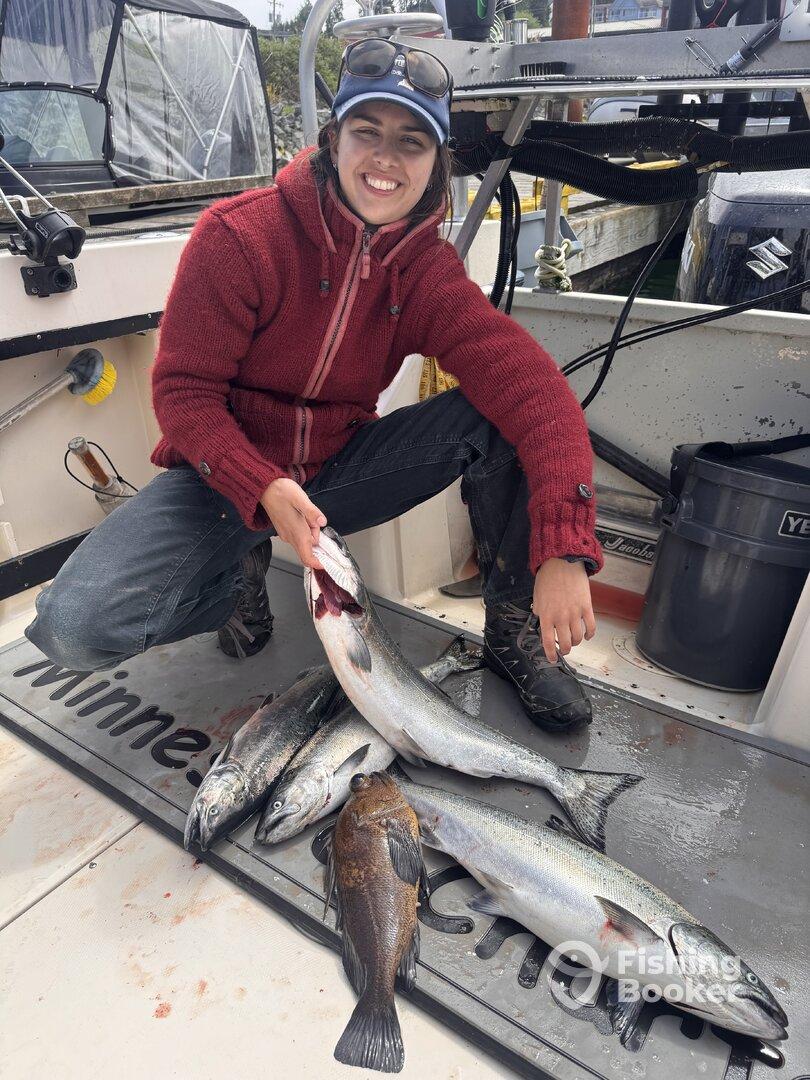 A young angler proudly displaying a catch of salmon and rockfish aboard a fishing boat.