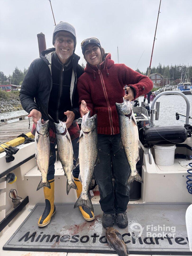 Two anglers proudly displaying their catch of Salmon on a fishing charter in a scenic harbor.