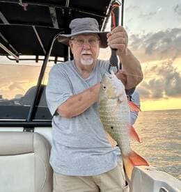 An angler proudly displaying a large Snapper caught during a sunset fishing trip on a boat.