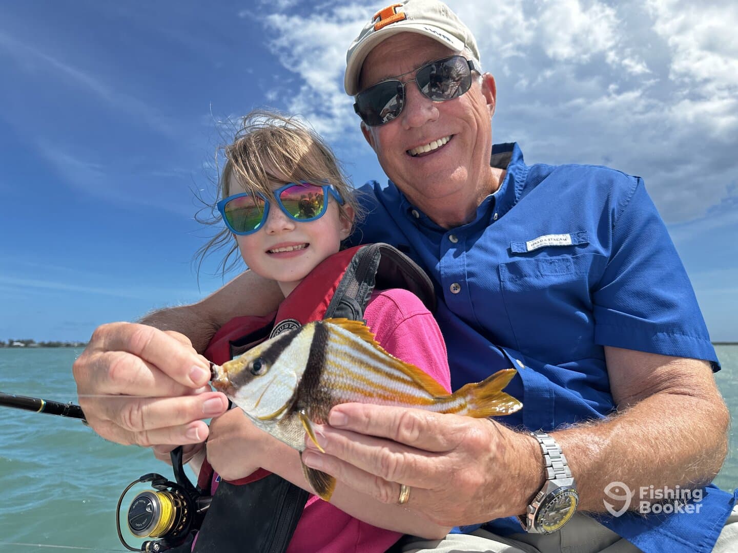 A young girl and her grandfather proudly display a colorful fish while enjoying a sunny day on the water.