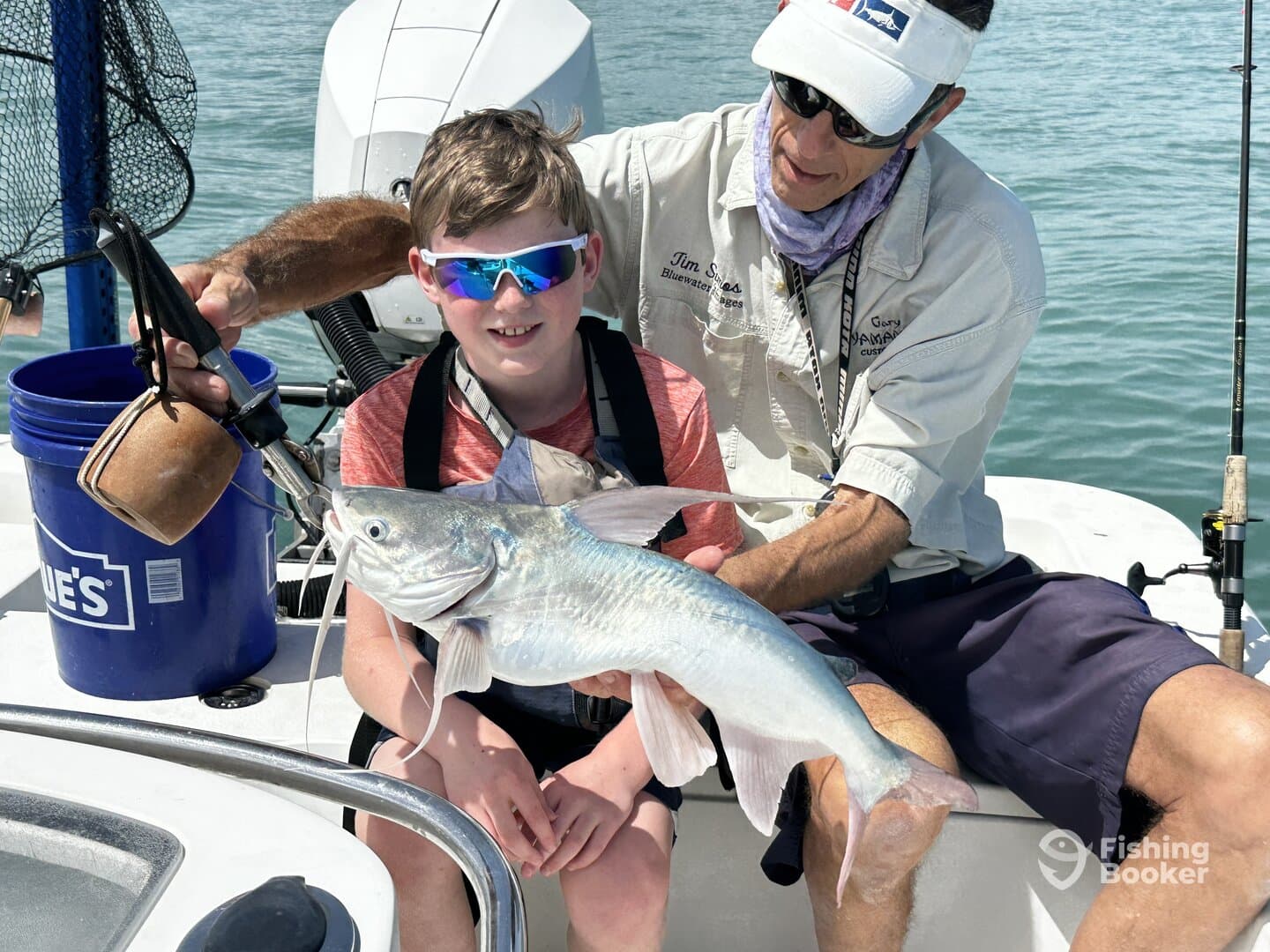 A young angler proudly displays a large catfish while fishing with a guide on a sunny day.