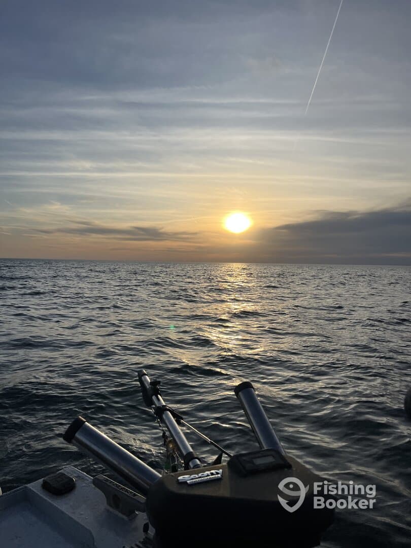 A serene sunset view over the ocean, showcasing the side of a fishing boat with rod holders, perfect for an evening fishing trip.