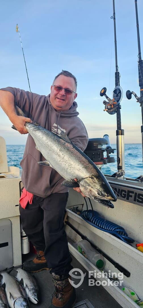 Angler proudly displaying a large Salmon aboard a fishing boat, showcasing a successful day on the water.