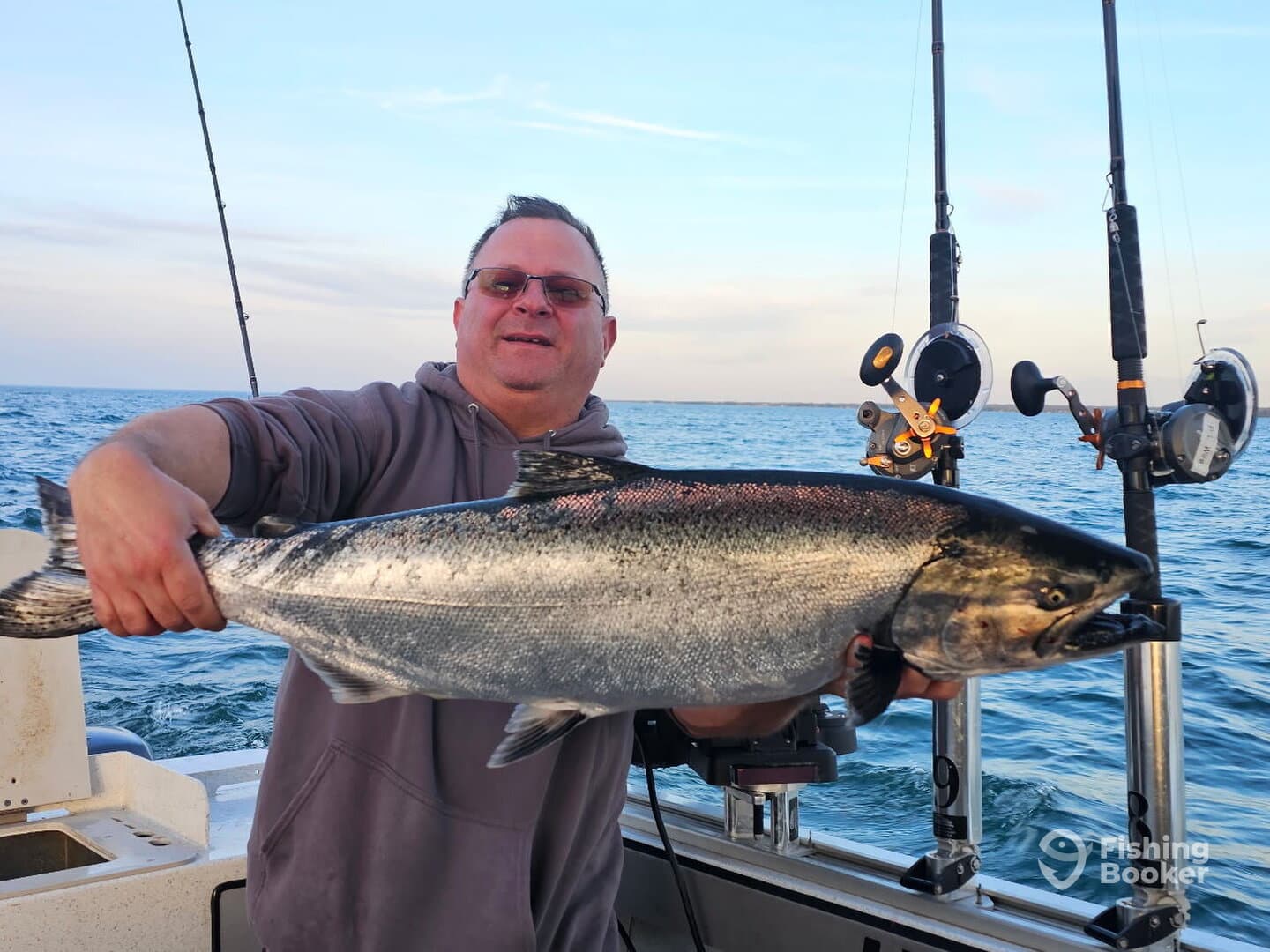 Angler proudly displaying a large Salmon while fishing on a boat, showcasing a successful day on the water.