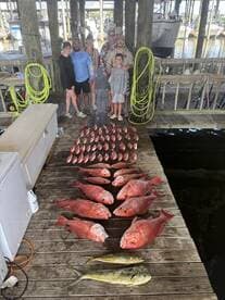 A family group proudly displays a successful catch of red snapper and mahi-mahi on the dock after a fishing trip.