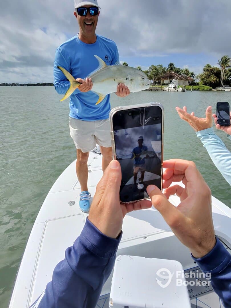A proud angler displaying a large Jack Crevalle while friends capture the moment on their phones during a fishing trip.