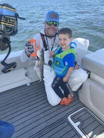 A proud angler and a young boy display a freshly caught fish aboard a boat, showcasing a fun family fishing experience.