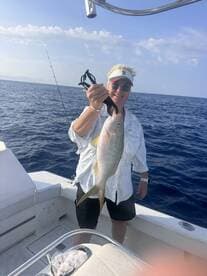 Angler proudly displaying a large Yellowtail Snapper while fishing on a boat in open waters.