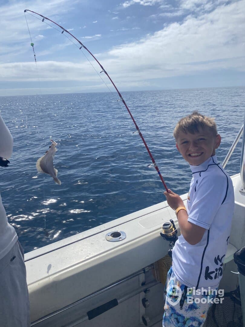 A young angler joyfully reeling in a fish while fishing on a boat in open waters, showcasing the excitement of the catch.