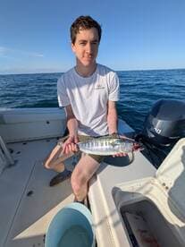 A young angler proudly displaying a freshly caught fish while on a boat in open waters.