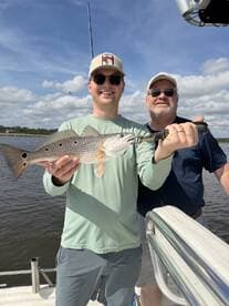 Two anglers proudly displaying a Redfish on a boat during a sunny fishing trip.