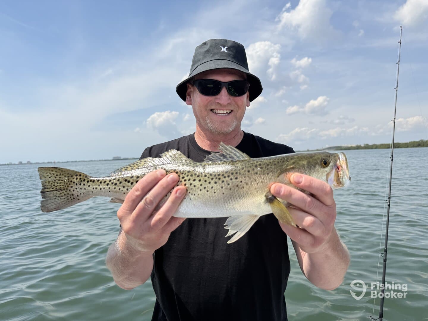 Angler proudly displaying a large Speckled Trout while fishing in a scenic coastal environment.