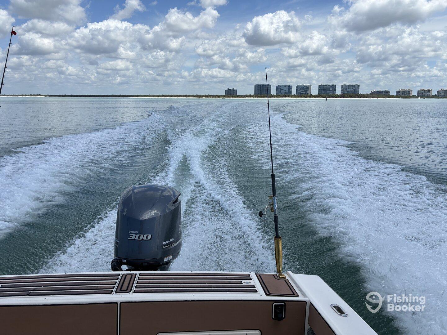 A scenic view from the back of a boat, showcasing the powerful Yamaha 300 engine and the calm waters, with buildings lining the shore in the background.