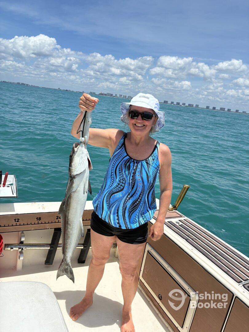 A smiling angler proudly displaying a large fish while fishing on a sunny day in coastal waters.