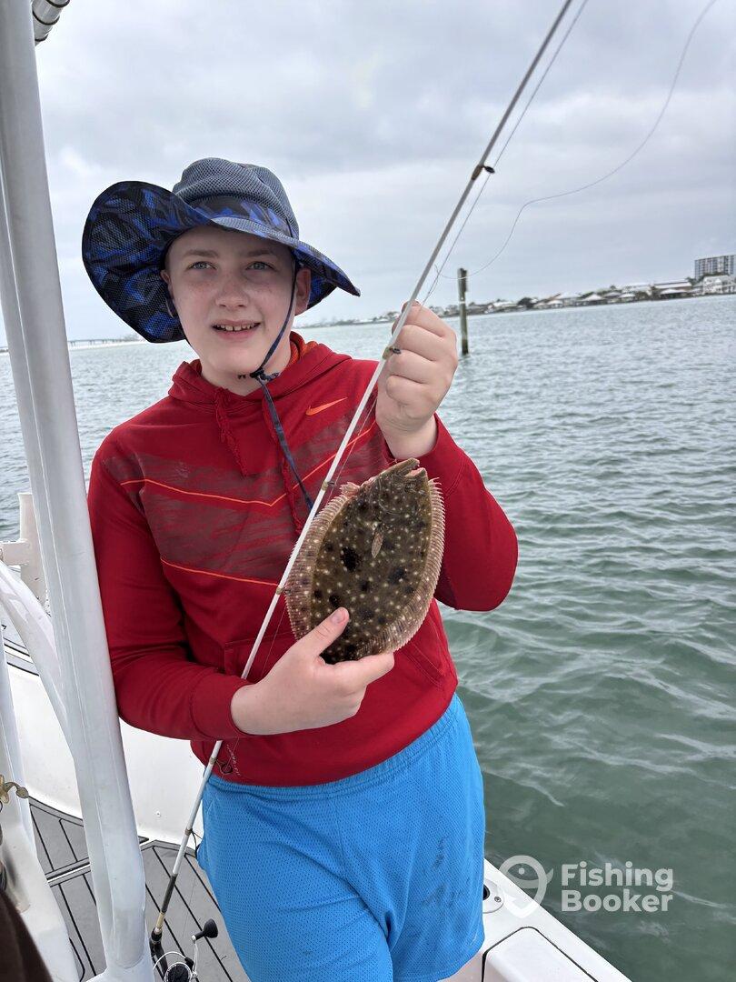 A young angler proudly displaying a caught Flounder while fishing from a boat in a coastal waterway.