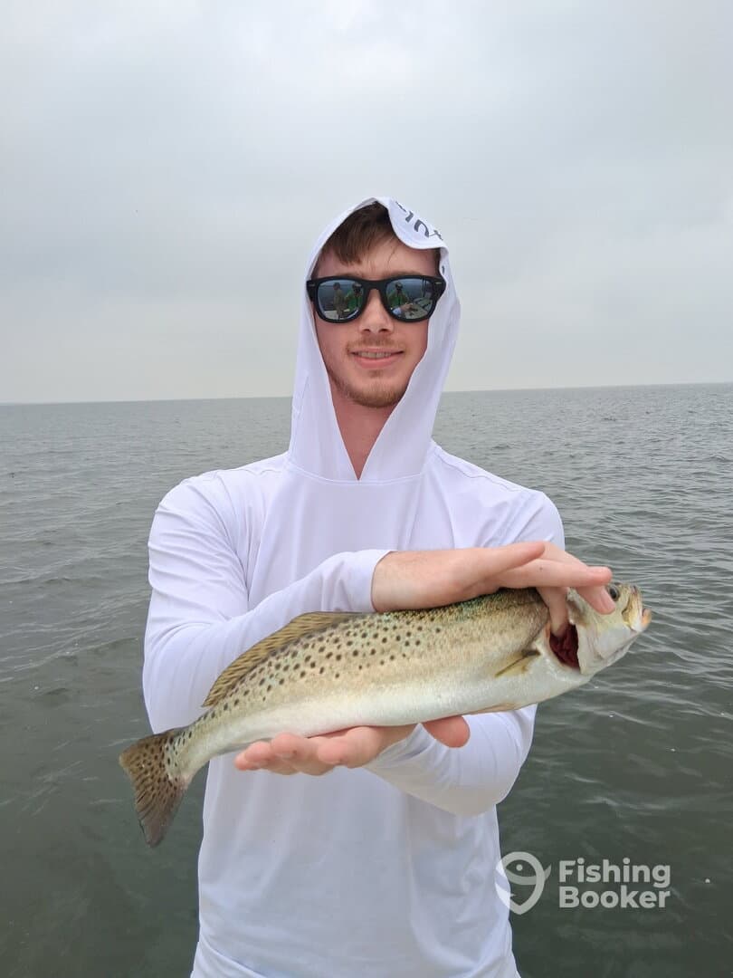 A young angler proudly displaying a Speckled Trout while fishing on a cloudy day.