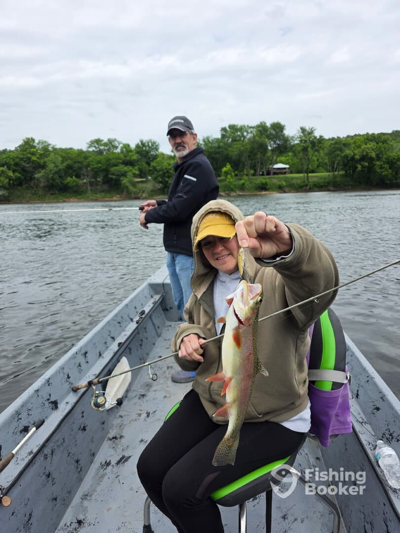 A young angler proudly displaying a freshly caught Largemouth Bass while fishing from a small boat on a calm river.