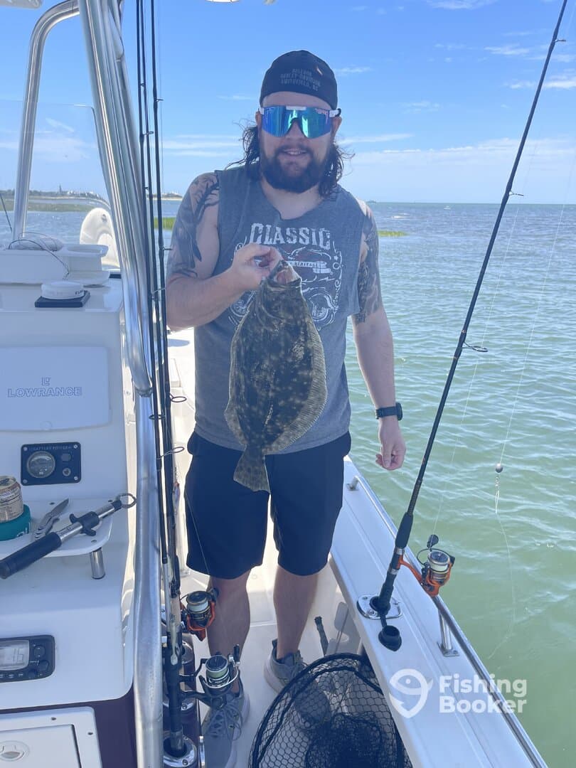 Angler proudly displaying a Flounder while fishing on a boat in coastal waters.