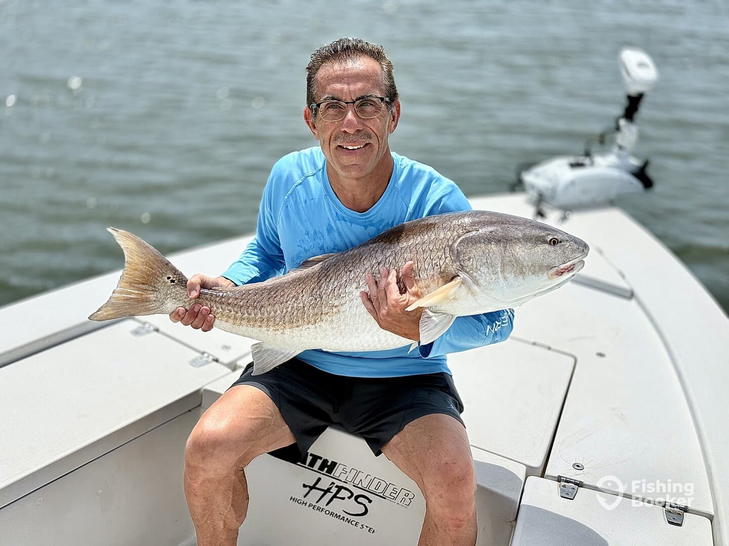 An angler proudly displaying a large Redfish while sitting on a boat, showcasing a successful day of fishing.