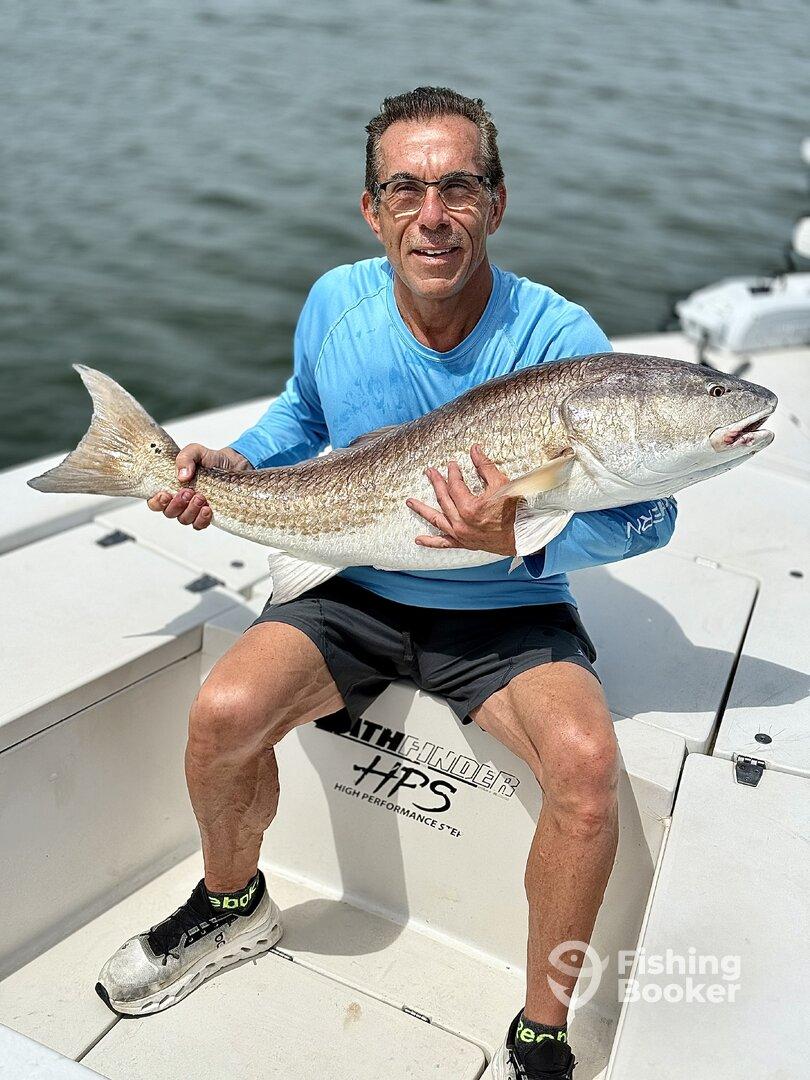An angler proudly displays a large Redfish while seated in a boat, showcasing a successful day on the water.
