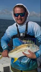 Angler proudly displaying a large Yellowtail at sea, showcasing a successful fishing trip.