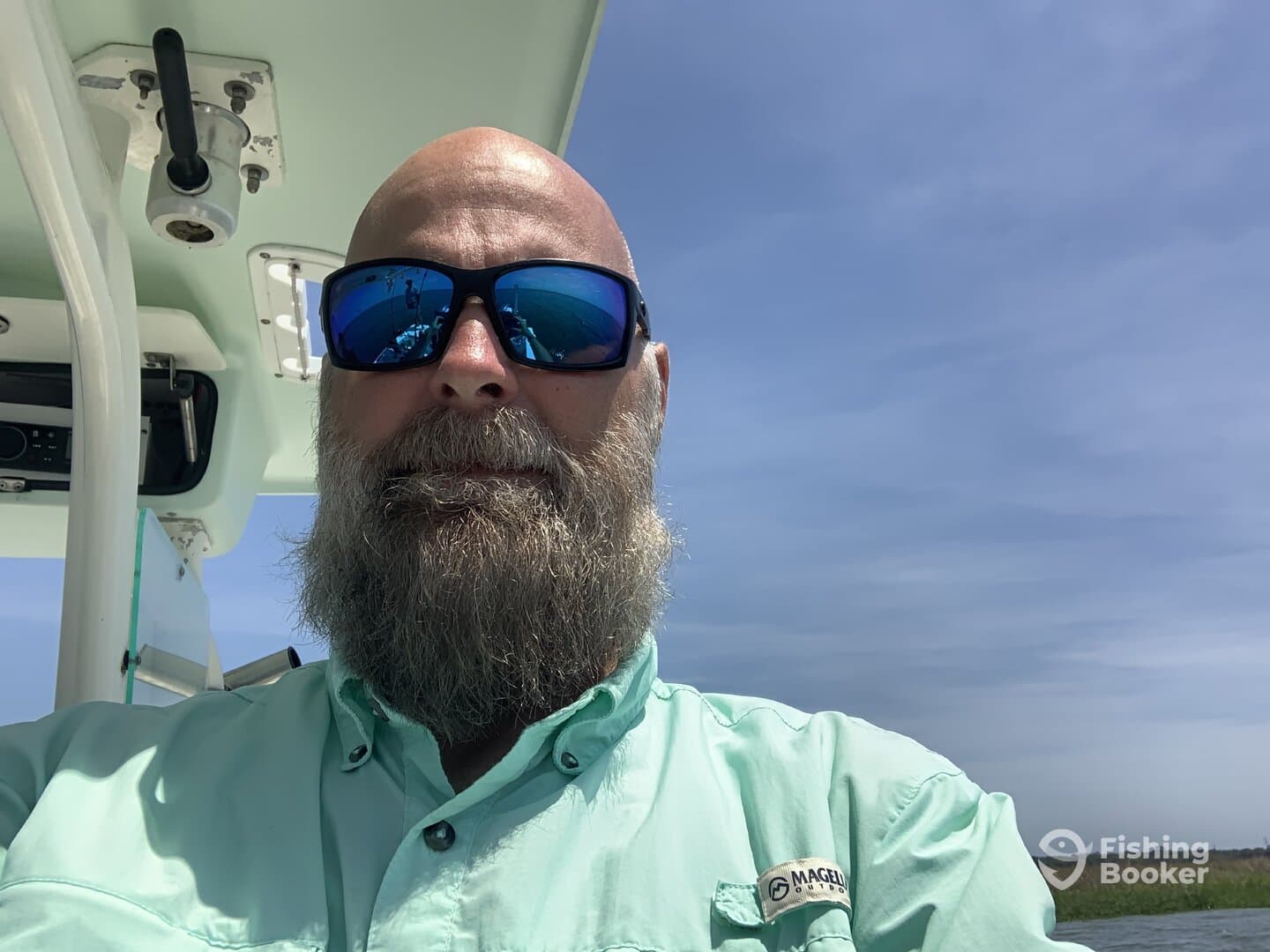 A bearded angler takes a selfie inside the boat, showcasing the helm area and clear blue skies.