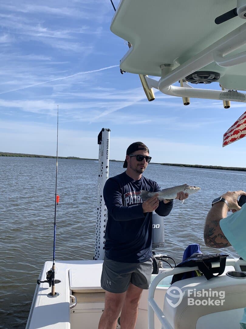 Angler holding a Speckled Trout on a boat in a scenic fishing environment.