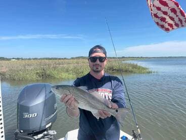 Angler proudly displaying a striped bass while fishing in a scenic coastal environment.