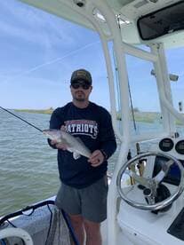 Angler holding a freshly caught Speckled Trout aboard a fishing boat in a coastal waterway.