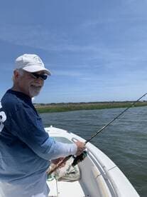An angler casting a line from a boat on a sunny day, surrounded by lush greenery and calm waters.