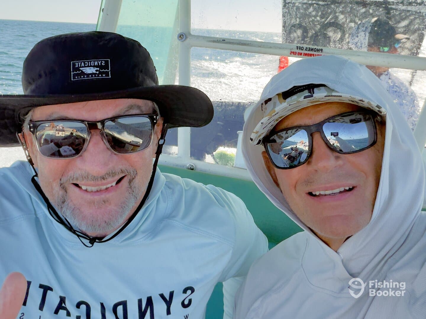 Two anglers enjoying a day on the water, seated inside the boat with a scenic ocean backdrop.