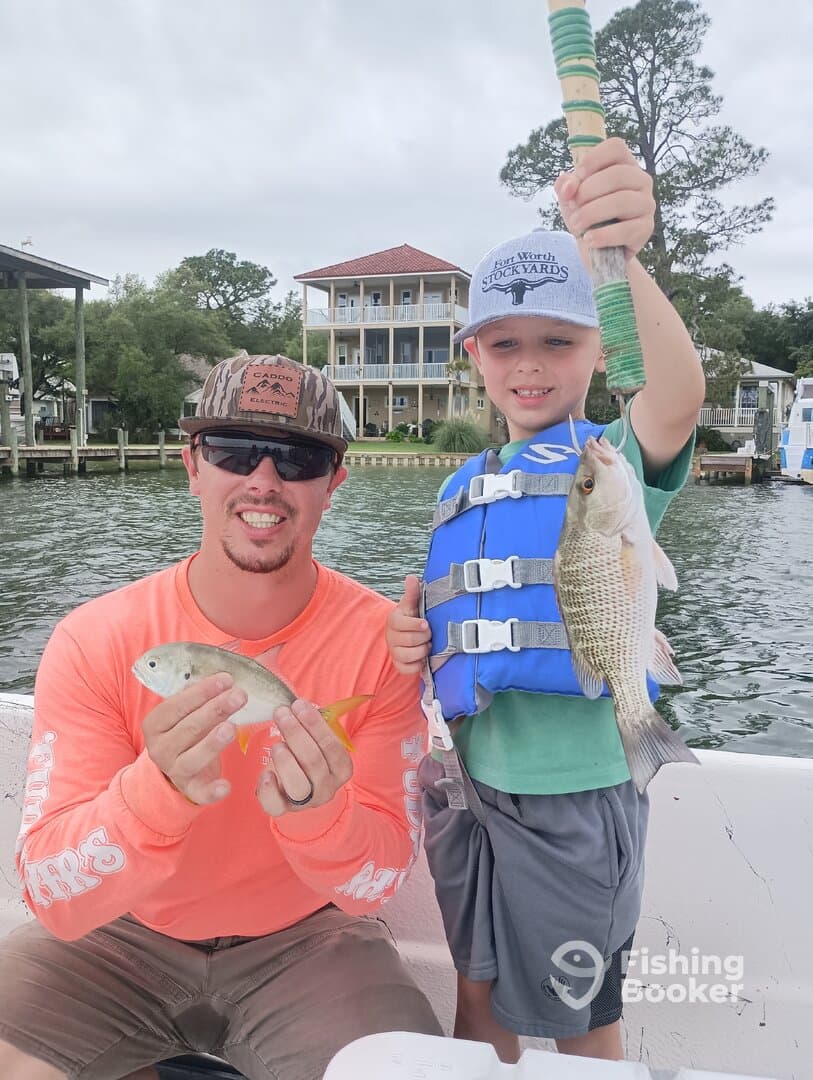 A proud young angler holding a fish alongside an adult, both enjoying a fishing trip on the water.