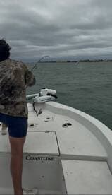 A young angler is actively reeling in a fish while fishing from a Coastline boat, with a cloudy sky in the background.