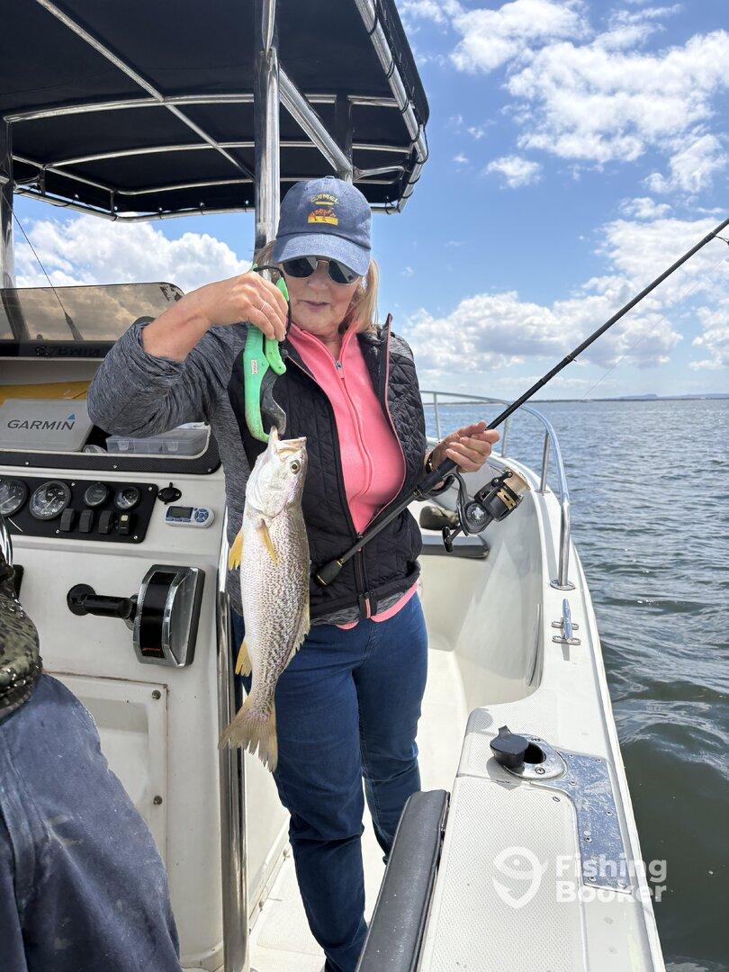 A woman proudly displaying her catch, a Speckled Trout, while fishing on a boat.