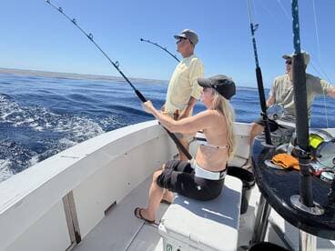 A group of anglers actively fishing on a boat, with one person reeling in a catch while enjoying a sunny day on the water.