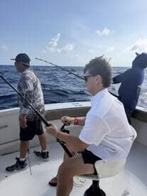 A young angler actively reeling in a fish while two companions assist on a sport fishing boat in open water.