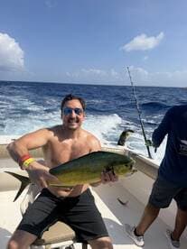 Angler proudly displaying a vibrant Mahi Mahi while fishing on a boat in open waters.