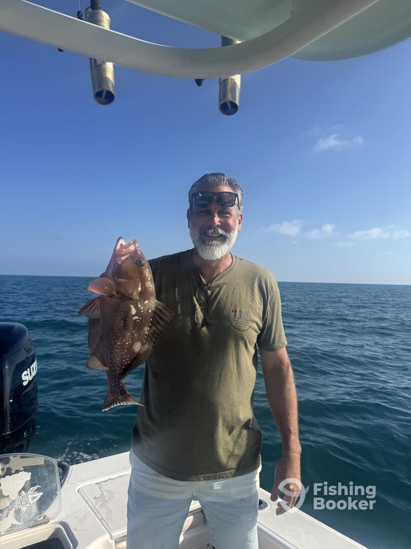 Angler proudly displaying a large Grouper while fishing on a boat in open waters.