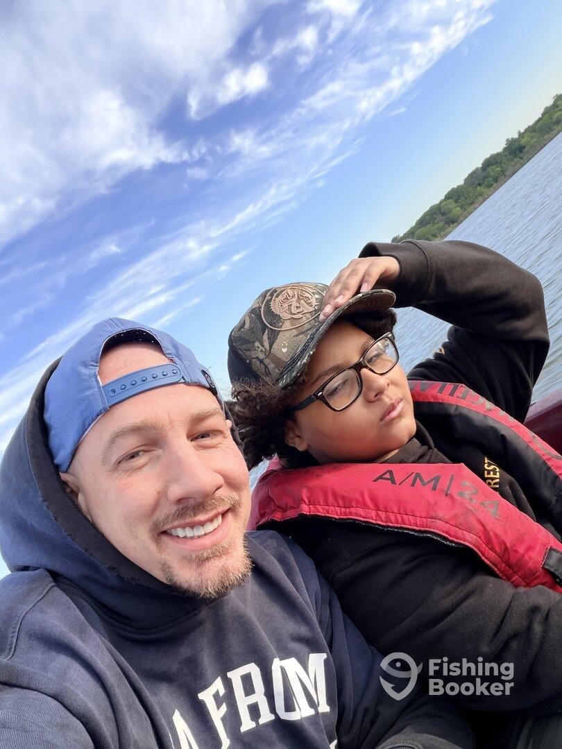 Two individuals enjoying a day on the water, with one wearing a life jacket. The setting appears to be a fishing trip.