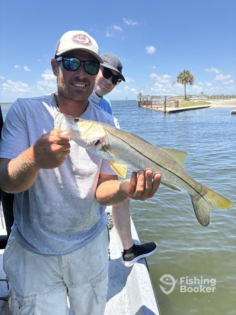Angler proudly displaying a Snook caught during a fishing trip, with a scenic waterfront in the background.