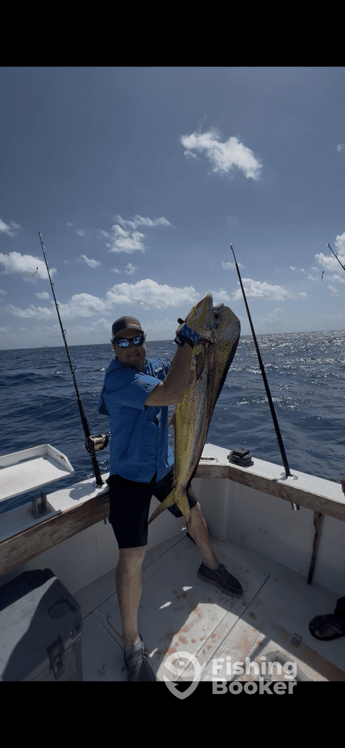 Angler proudly displaying a large Mahi Mahi aboard a fishing boat in open waters, showcasing a successful deep-sea fishing trip.