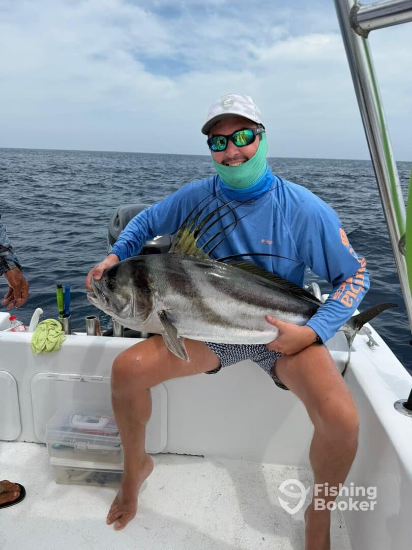 A proud angler displaying a large Roosterfish while fishing on a boat, showcasing a successful day on the water.