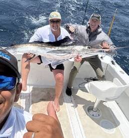 Two anglers proudly displaying a large Swordfish on a fishing charter, enjoying a sunny day on the water.