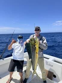 Two anglers proudly displaying a large Mahi Mahi on a fishing charter in open waters.