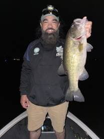 Angler proudly displaying a large Largemouth Bass while fishing at night from a boat.