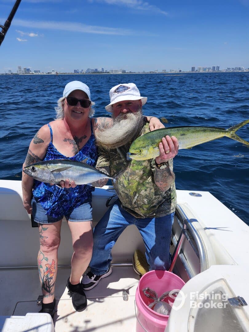 Two anglers proudly displaying their catch, a Mahi Mahi and a Bluefish, while enjoying a sunny day on the water.