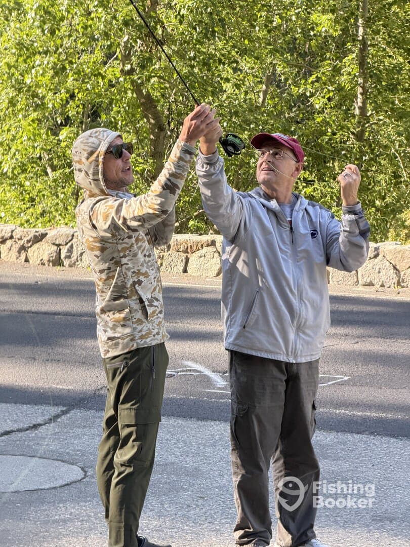 Two anglers engaged in casting technique, showcasing a moment of learning and collaboration in a scenic outdoor setting.