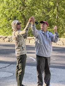 Two anglers engaged in casting technique, showcasing a moment of learning and collaboration in a scenic outdoor setting.