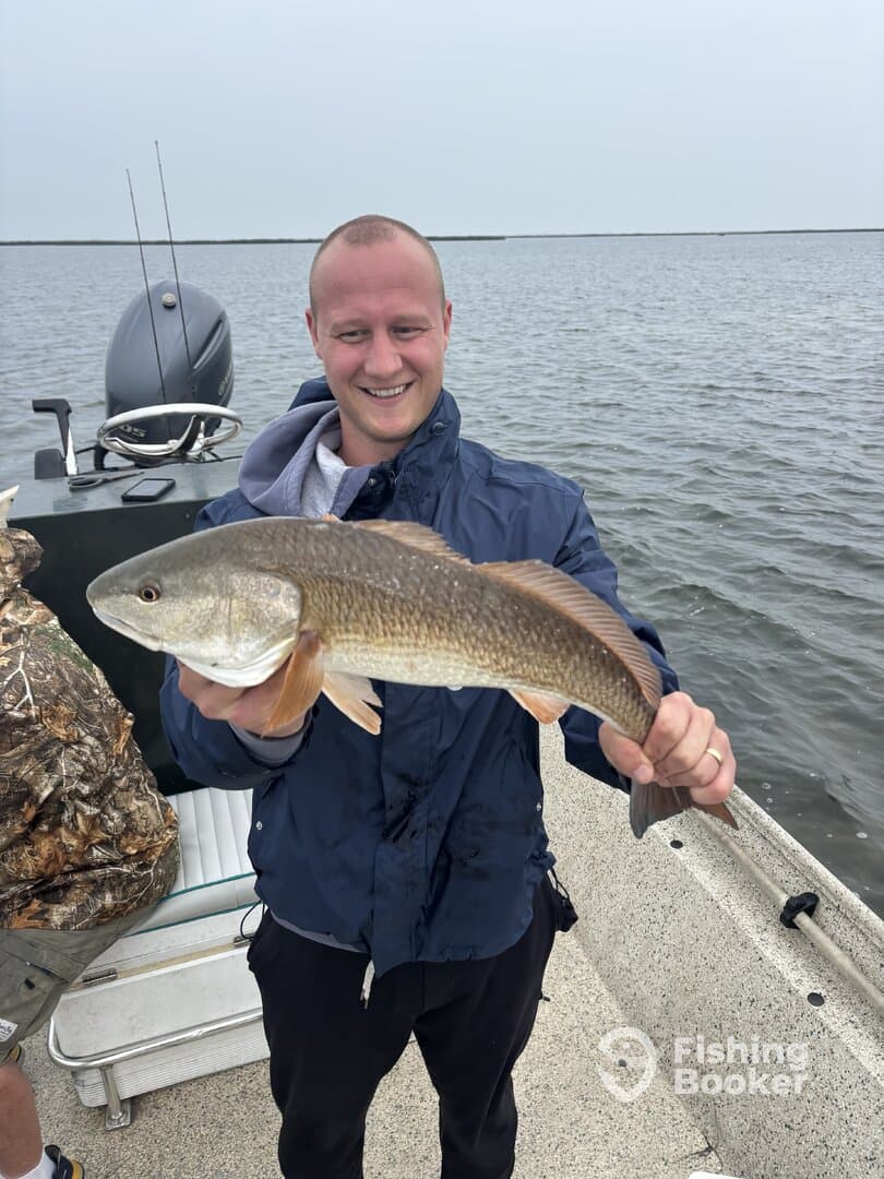 Angler proudly displaying a Redfish while fishing from a boat in a coastal waterway.